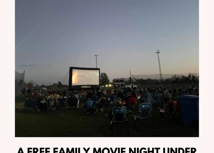 Large group of people in lawn chairs watching a movie on a screen outdoors at dusk